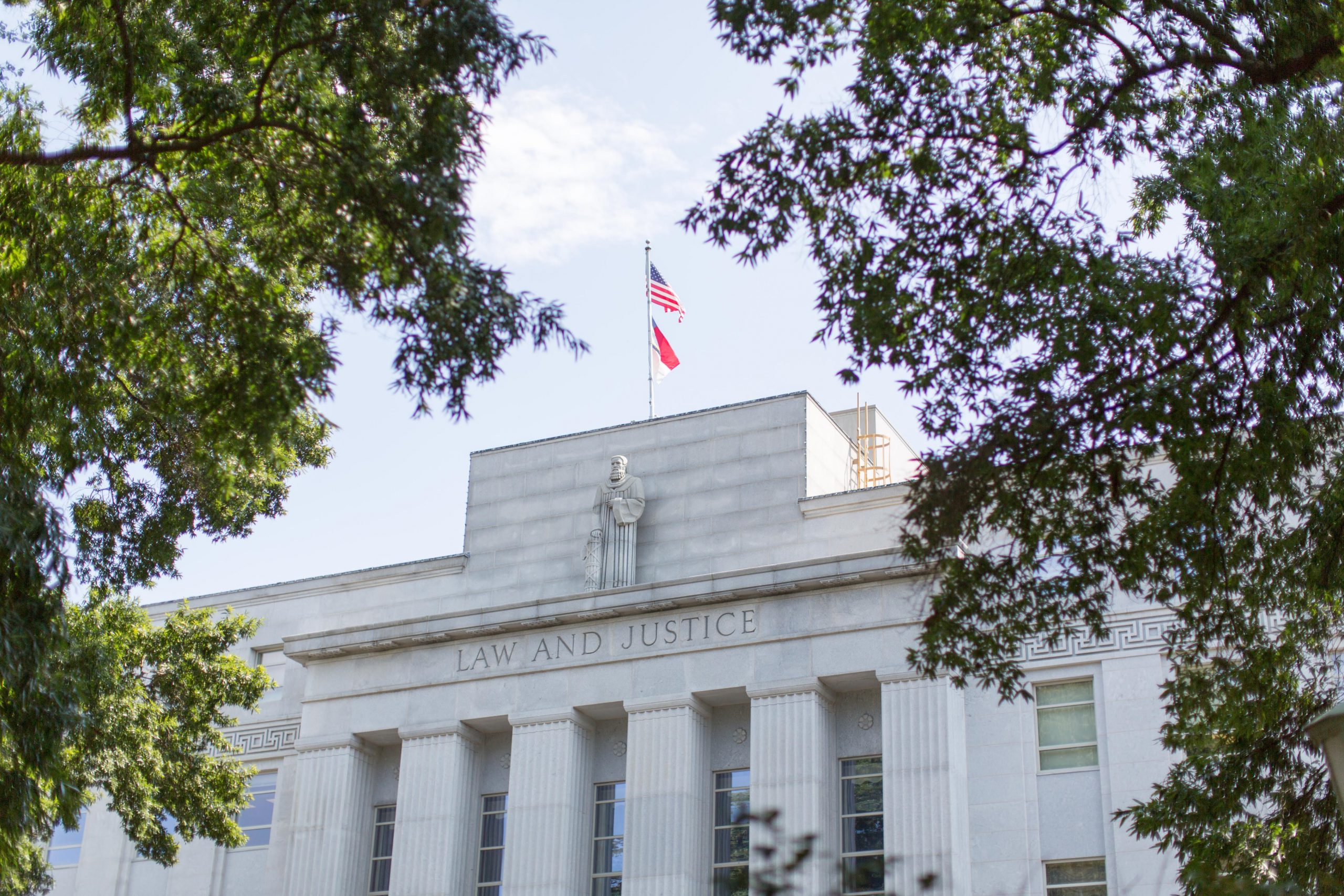 NC Supreme Court Building with American and State Flag, seen through the trees